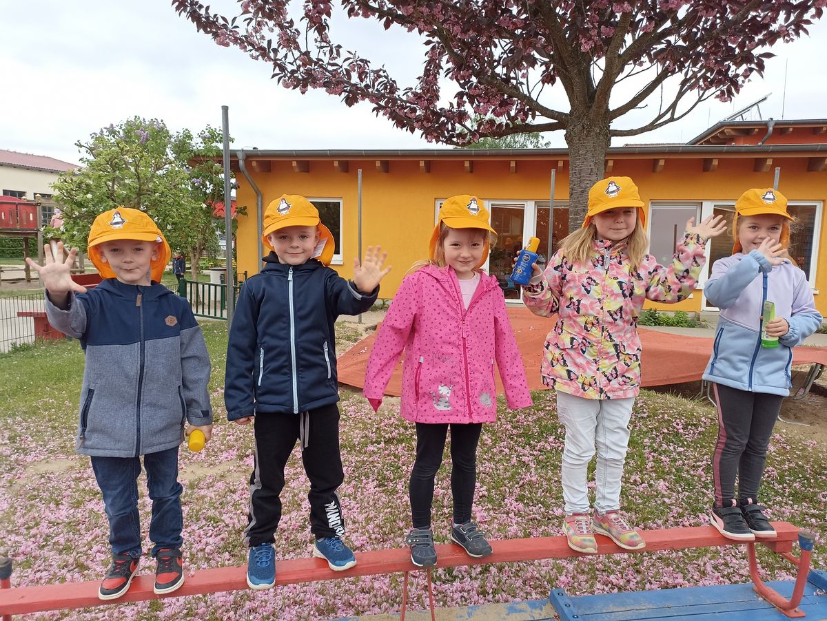 Lachende Kinder stehen mit Sonnenschutzkappen unter einem Baum.