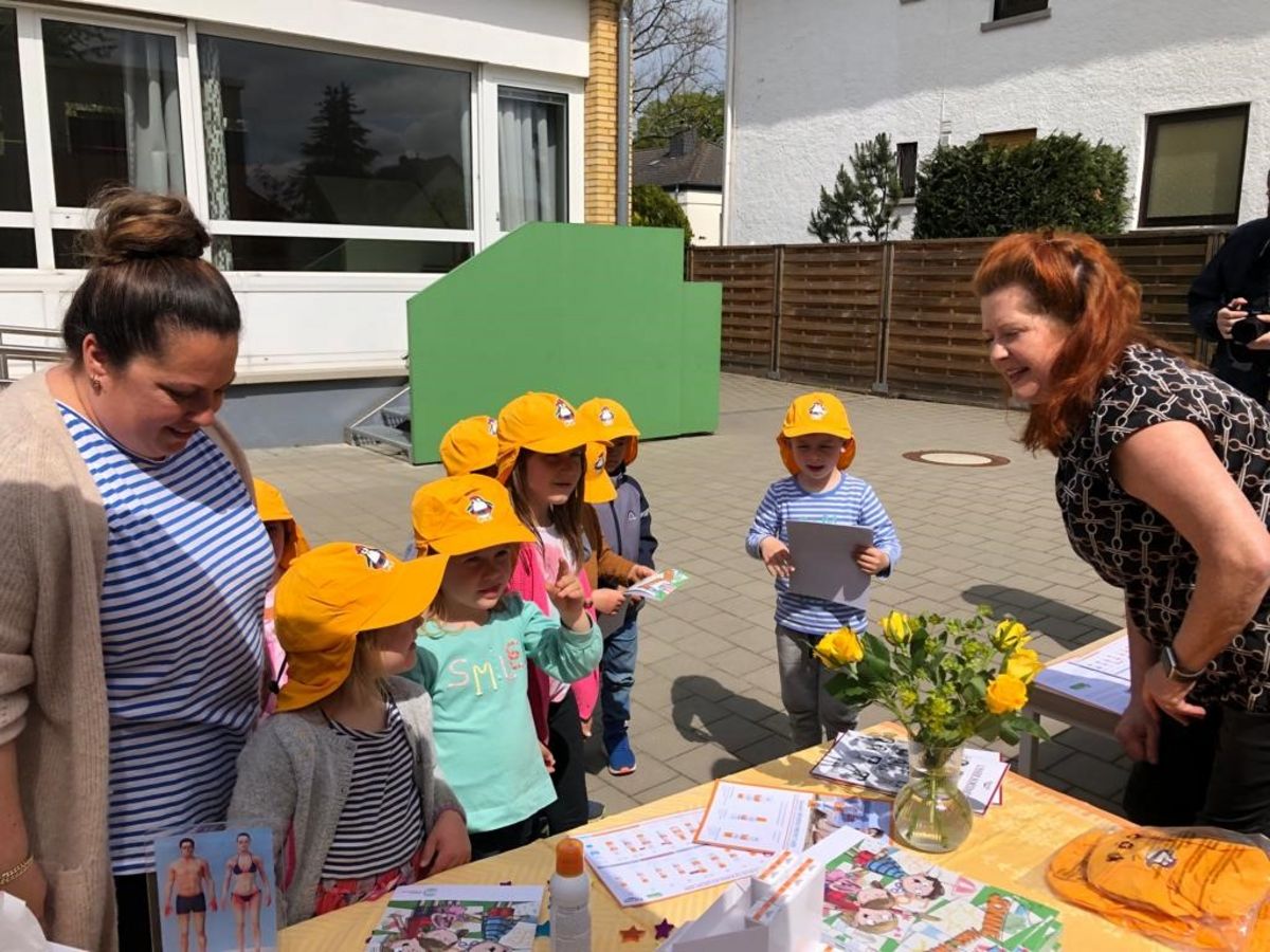 Kinder mit Sonnenschutzkappen stehen vor einem Tisch und erhalten Malblöcke.